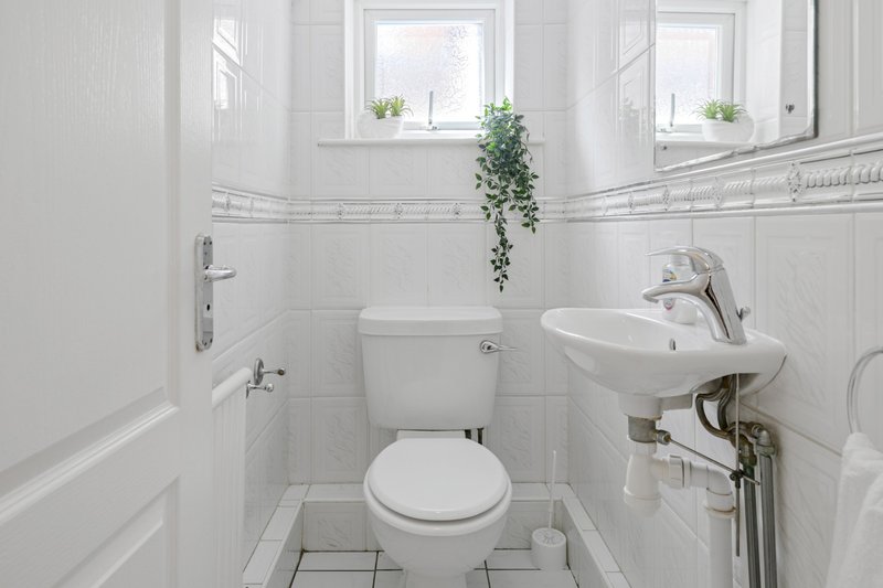 Clean white bathroom with toilet, wall-mounted sink, mirror and small window
