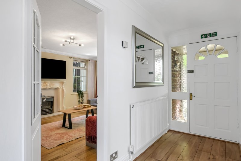 Bright entryway with white doors, mirror, radiator and wooden flooring leading to living room