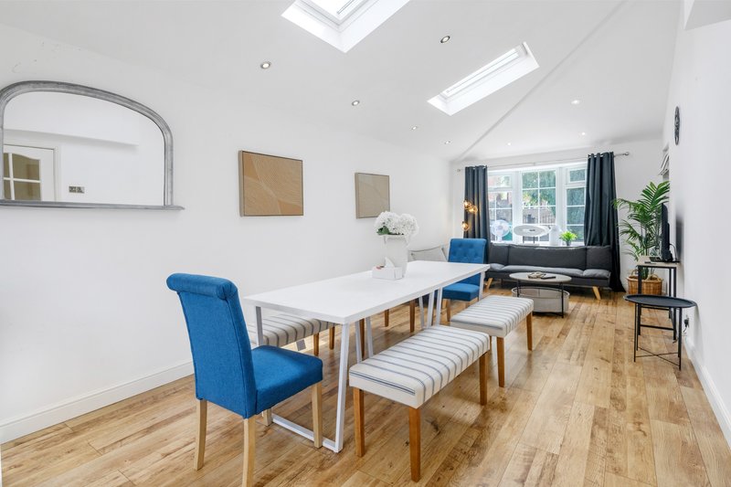 Bright modern dining room with white table, blue chairs, wooden flooring and skylights
