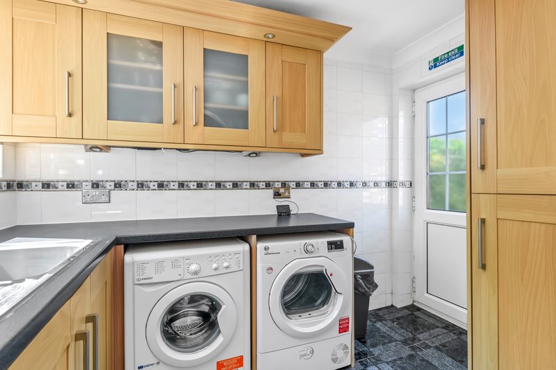 Utility room with wooden cabinets, washing machine, dryer, black countertop and door to garden