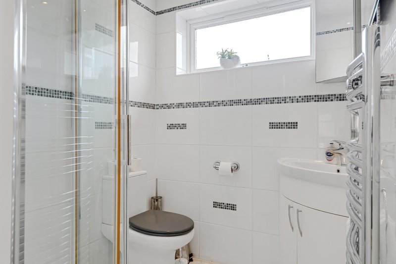 Modern bathroom with white tiles, glass shower enclosure, wall-mounted sink and mirror