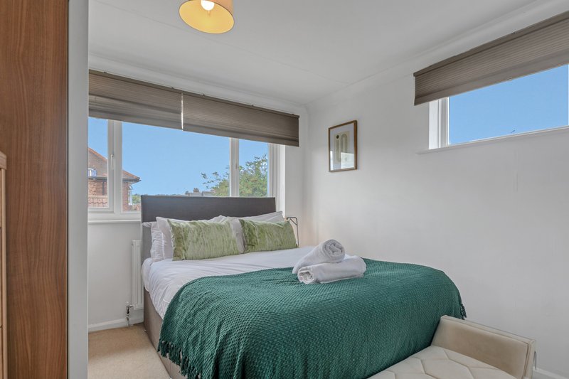 Bright bedroom with double bed, green bedding, white pillows and windows overlooking street