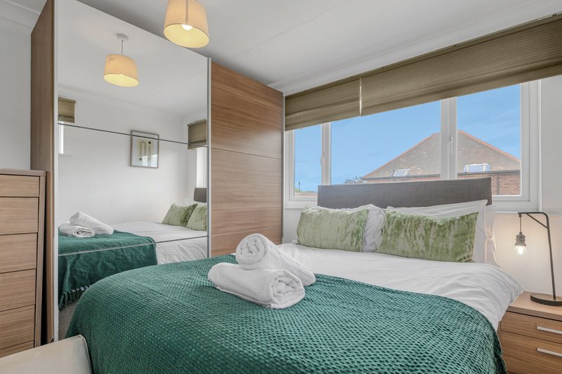 Modern bedroom with double bed, green bedding, rolled towels, and large window with street view