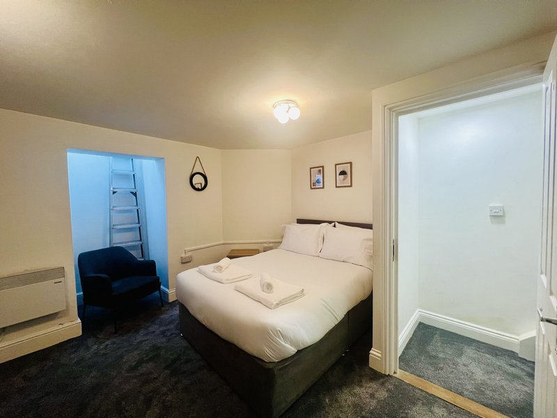 Bedroom with double bed, dark carpet, wall clock, and doorway to ensuite bathroom