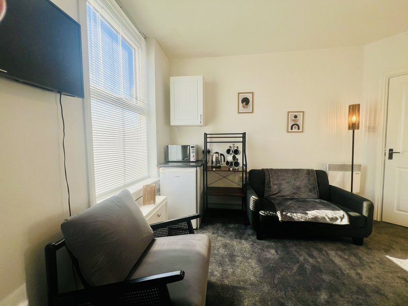 Living room with black sofa, armchair, TV, kitchenette, and window with blinds