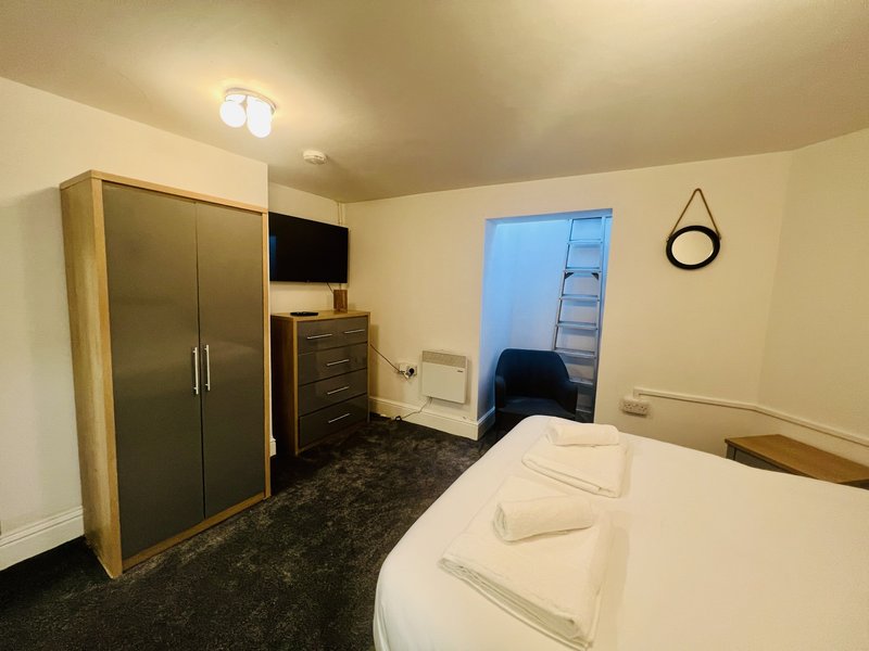 Bedroom with double bed, wardrobe, chest of drawers, wall-mounted TV and ensuite doorway