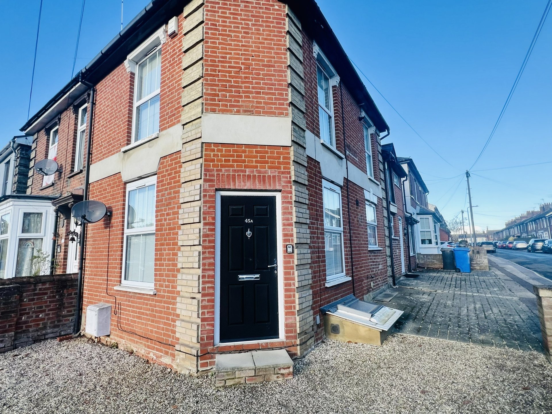 Red brick terraced house with black front door and white window frames, street view