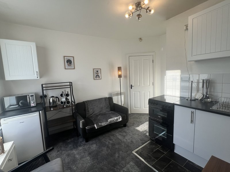 Open-plan kitchen and living area with black sofa, white cabinetry, and modern appliances