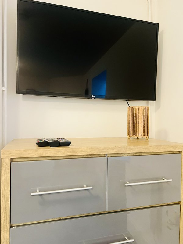 Wall-mounted flat-screen TV above wooden dresser with gray drawers and remote control