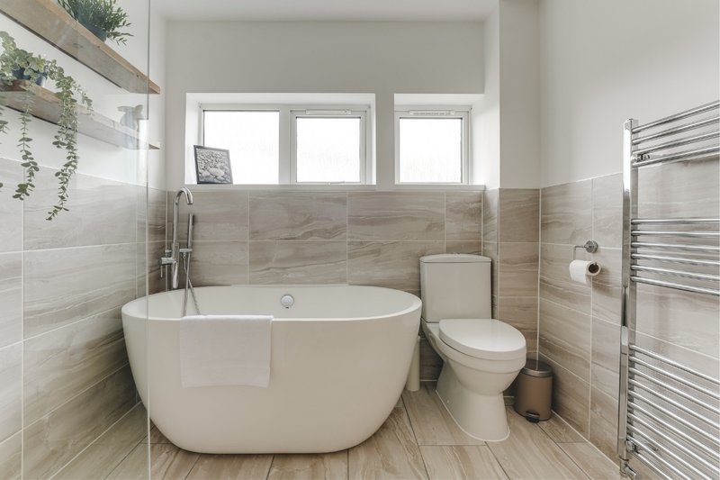 Modern bathroom with freestanding white bath tub, toilet, heated towel rail and window