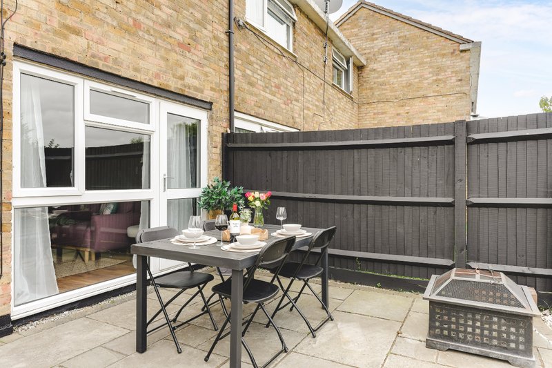 Patio area with dining table, chairs, flowers and grey fence beside brick house