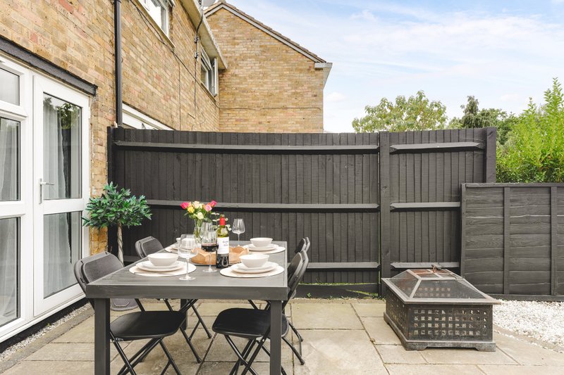Patio area with dining table, chairs, potted flowers, and dark wooden fence