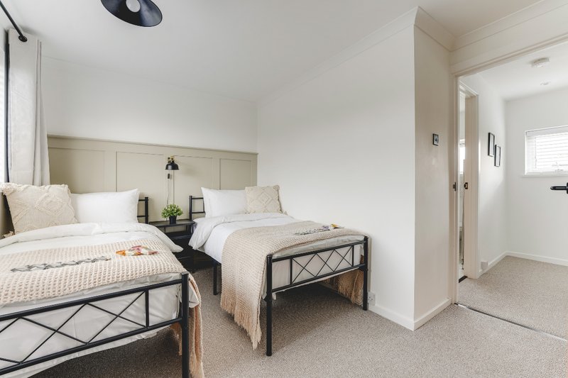Bright bedroom with two single beds, neutral bedding, wooden headboard, and ensuite bathroom door