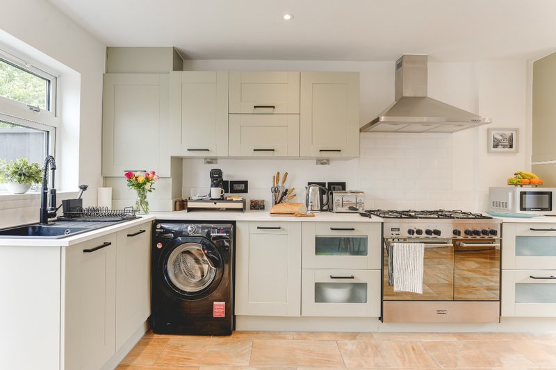 Modern cream kitchen with black washing machine, built-in oven, gas range and island with sink