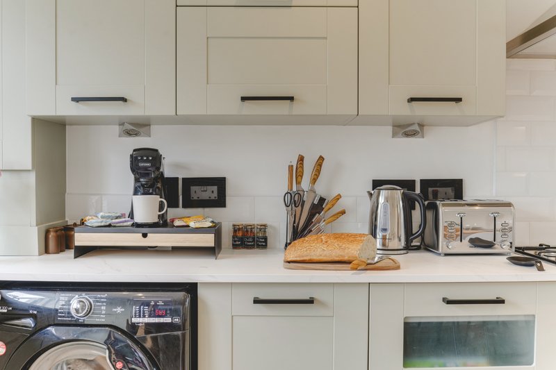 Modern kitchen with cream cabinetry, white countertop, appliances and cooking utensils