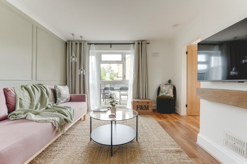 Modern living room with pink sofa, cushions, round coffee table, and glass doors opening onto balcony