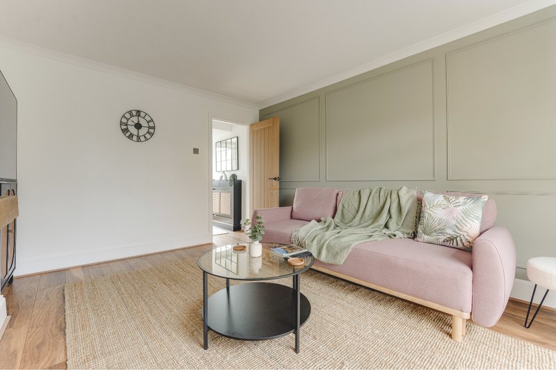 Modern living room with pink sofa, round coffee table, wooden floor and wall clock