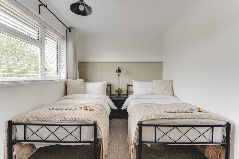 Twin bedroom with two single beds, neutral bedding, pendant light and window with blinds