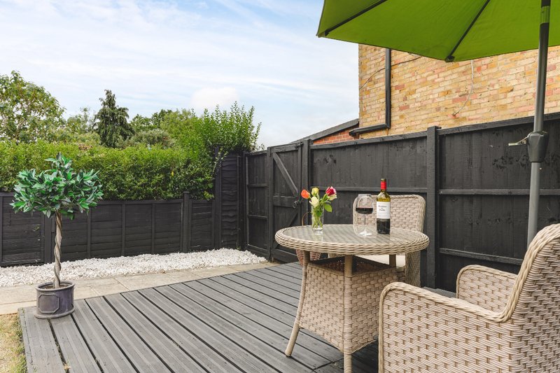 Outdoor patio with wooden decking, wicker furniture, green umbrella and garden seating area