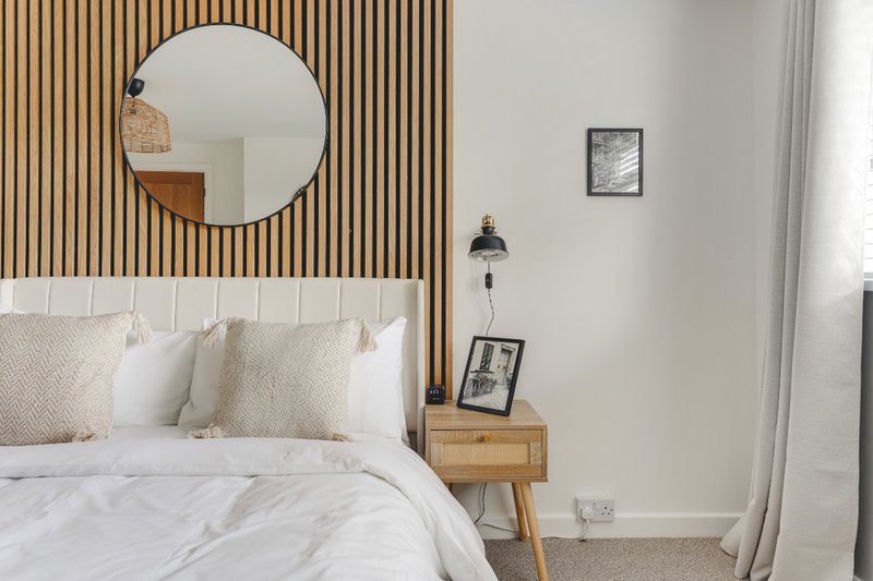 Modern bedroom with white bedding, round mirror, wood-slat headboard and wooden nightstand
