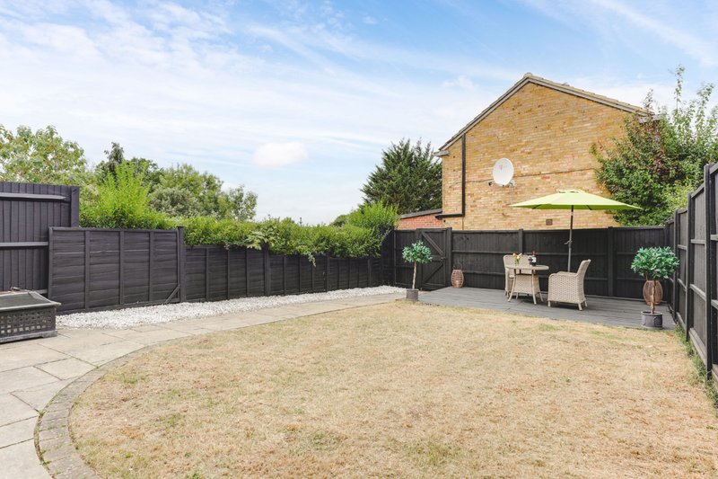 Spacious rear garden with paved patio, lawn, black fencing and brick house