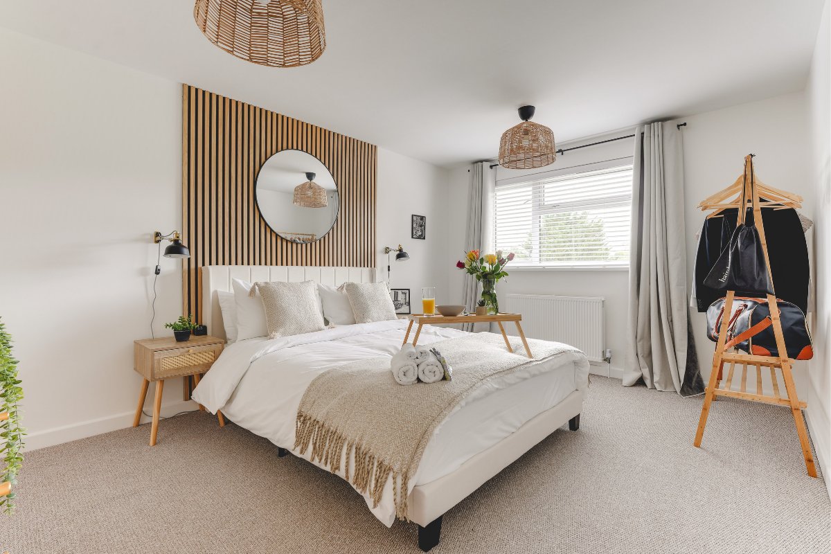 Bright bedroom with double bed, wooden headboard feature wall, round mirror, and wicker chair