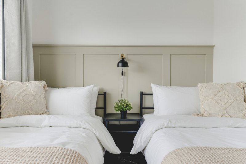 Twin bedroom with white bedding, beige patterned cushions, and shared nightstand with lamp