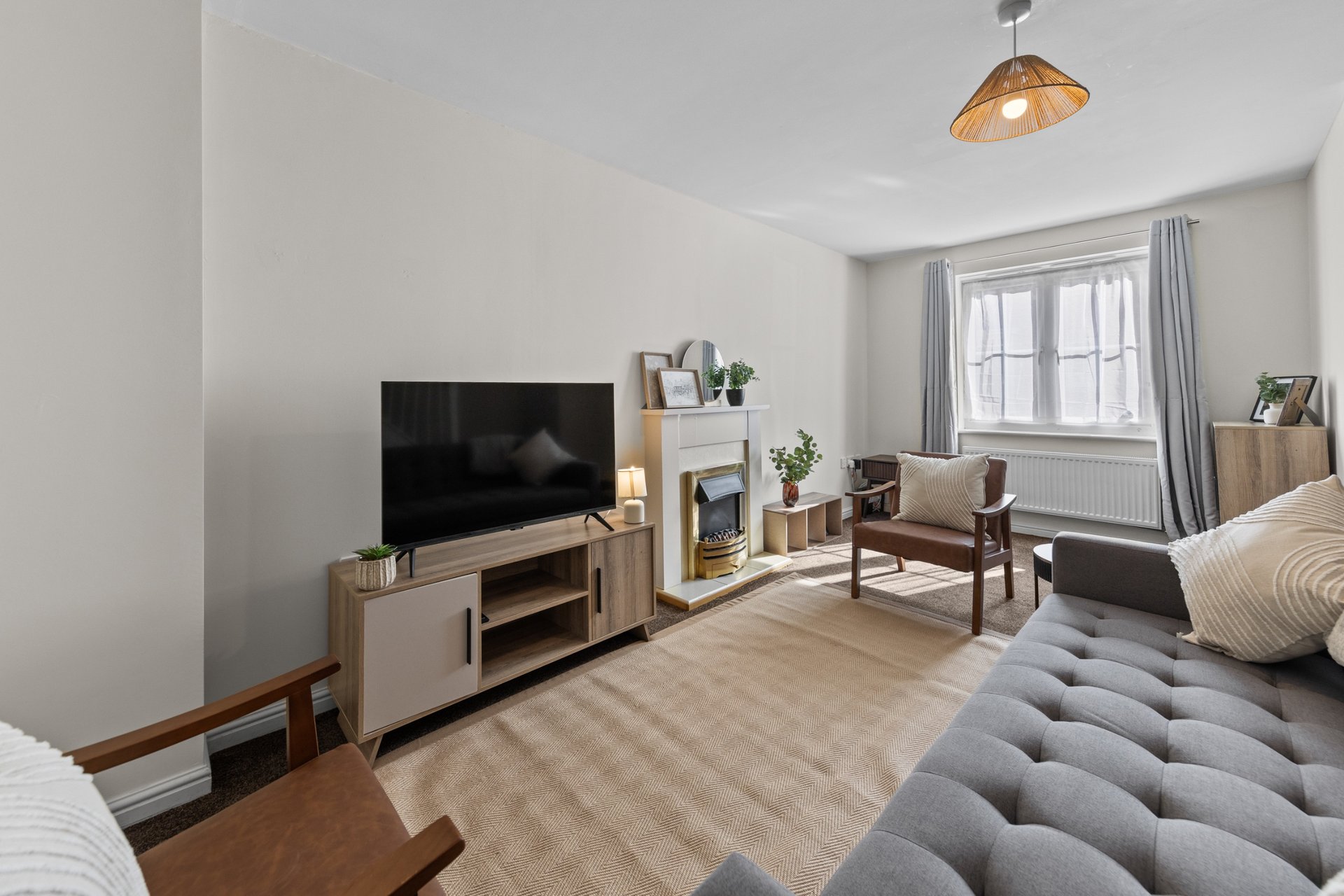 Spacious living room with TV, fireplace, gray sofa, armchair, wooden flooring and natural light