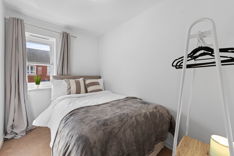 Bedroom with single bed, striped pillows, window with curtains, and coat stand