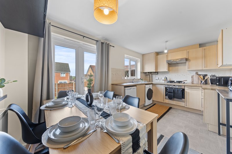 Open-plan kitchen and dining area with wooden table, place settings, and modern appliances