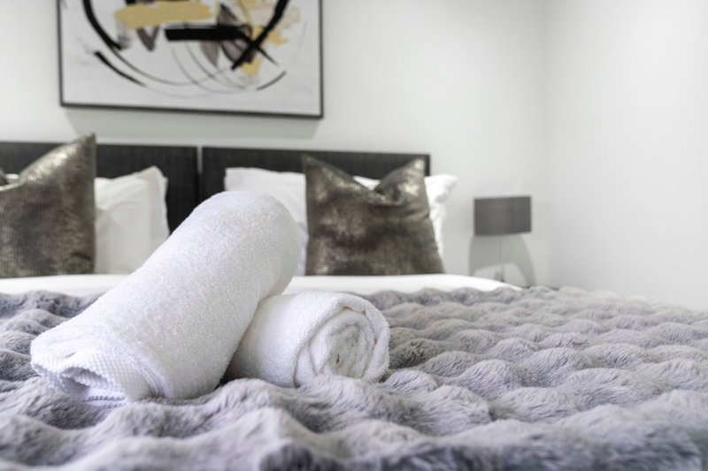 Modern bedroom with rolled towels on quilted bed and decorative pillows