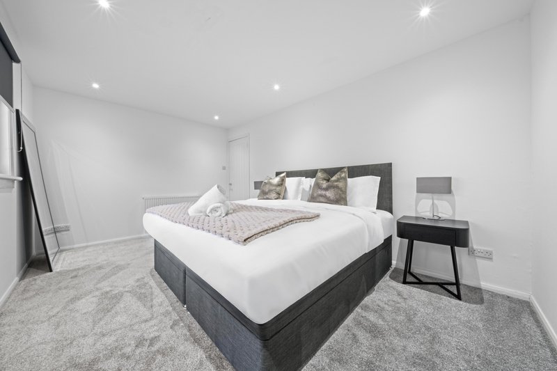 Modern bedroom with double bed, grey carpet, black nightstand and white walls