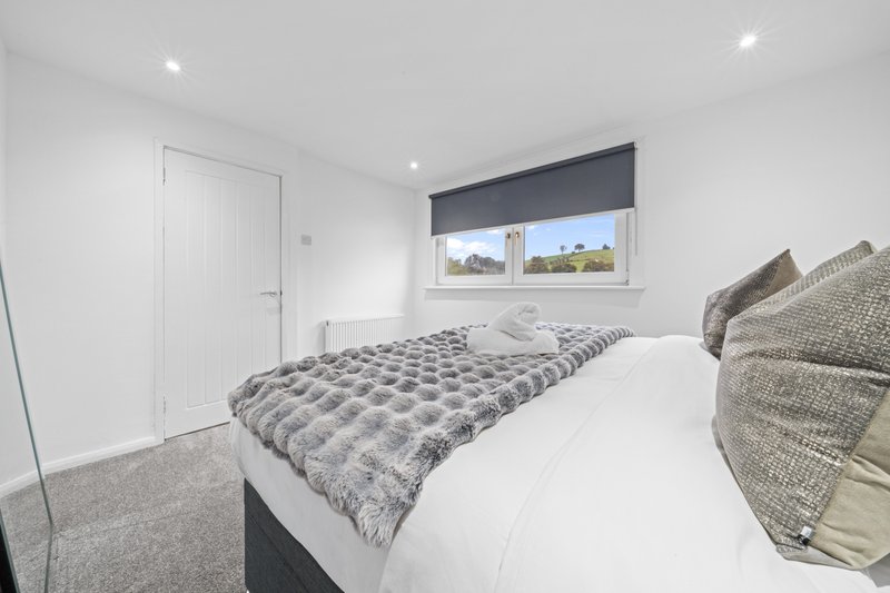 Modern bedroom with double bed, patterned bedding, grey cushions and window with blue blind