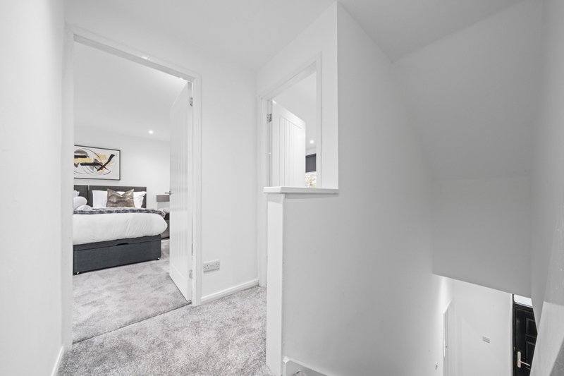 Modern hallway with grey carpet leading to bedroom with double bed visible through doorway