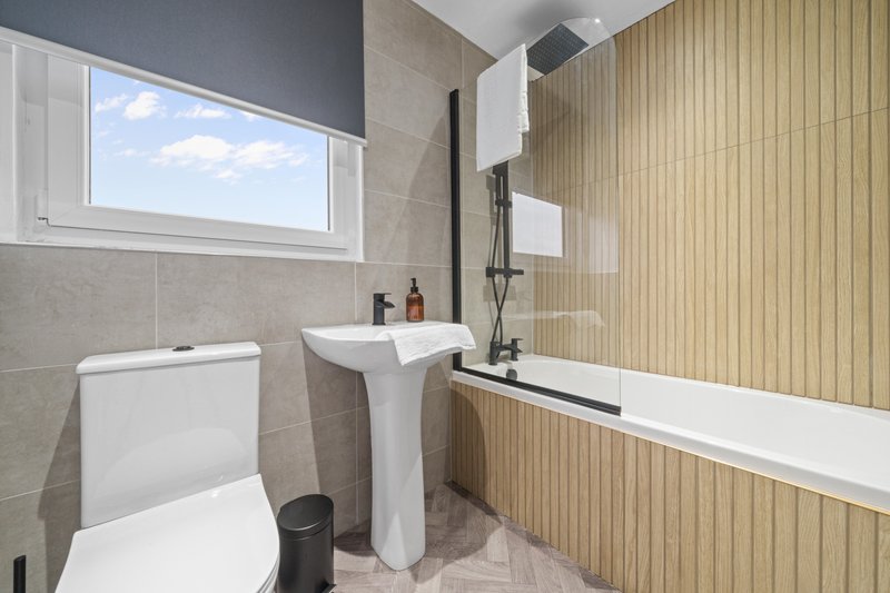 Modern bathroom with toilet, pedestal sink, bathtub, and window with natural light