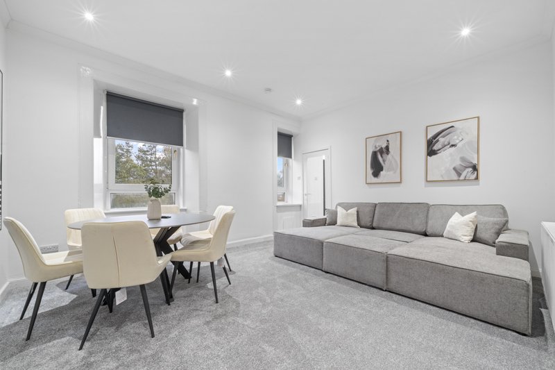 Open-plan living room with grey sofa, dining table, cream chairs and framed wall art