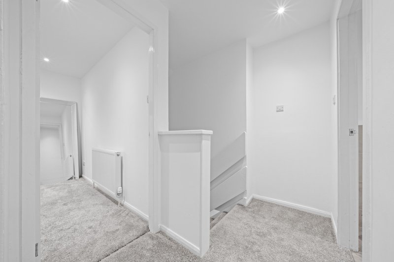 Modern hallway with carpeted floor, white walls, recessed lighting and multiple doors
