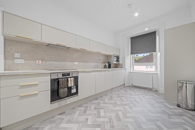 Modern kitchen with white cabinetry, beige backsplash, built-in oven and herringbone flooring