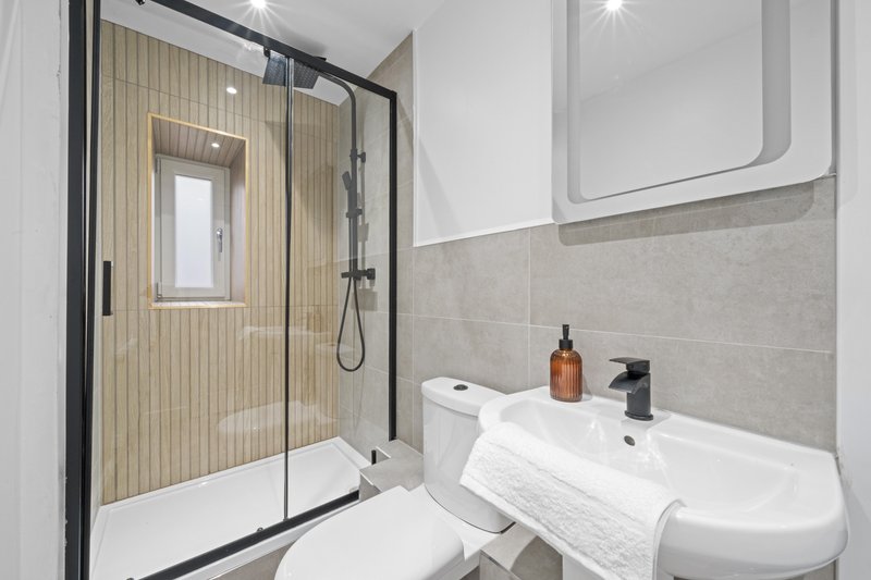 Modern bathroom with shower enclosure, white sink, toilet, and beige tile accents