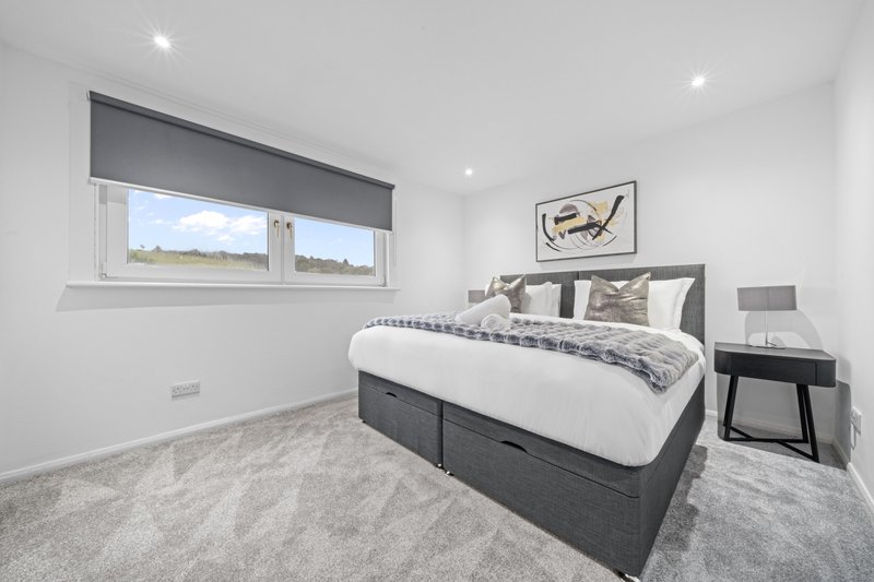 Modern bedroom with double bed, grey headboard, bedside table and window with rural view