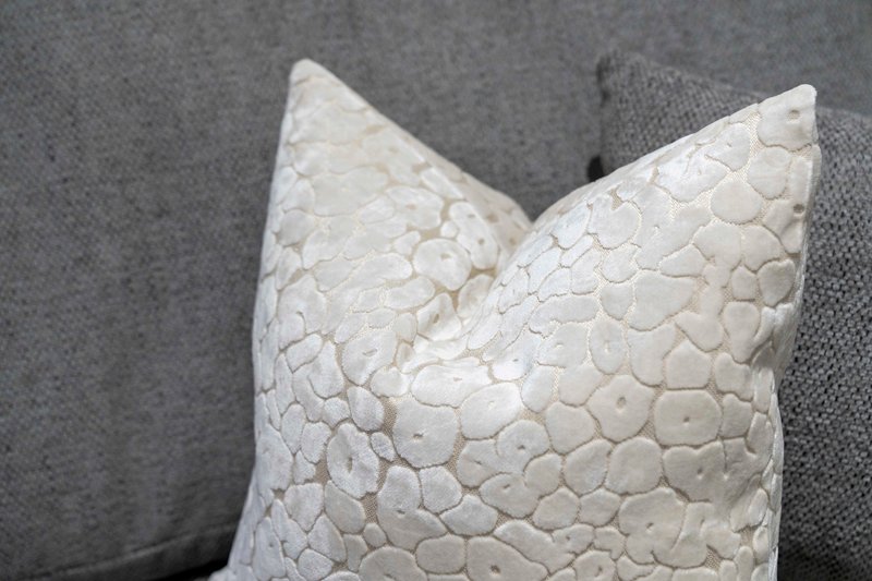 Close-up of white textured decorative cushion on gray upholstered furniture
