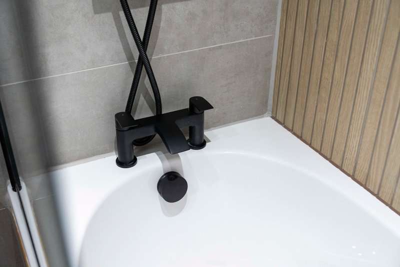 Modern bathroom bathtub with black contemporary faucet and gray tile surround