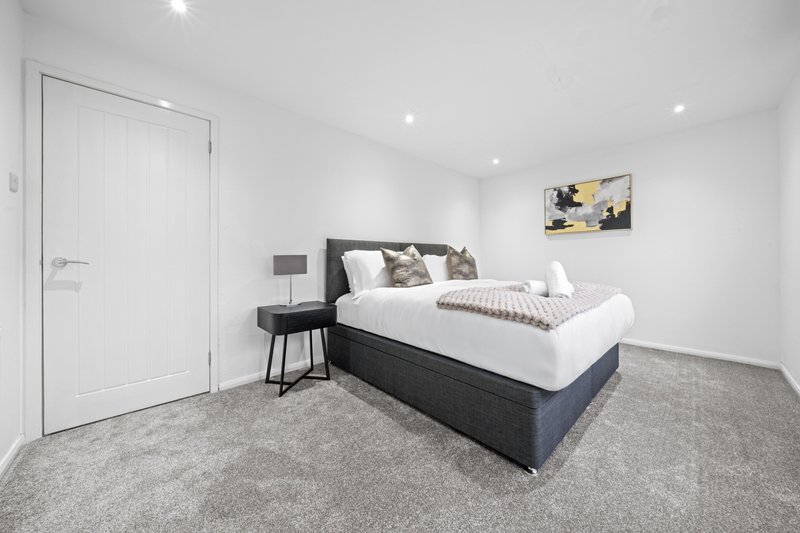 Modern bedroom with double bed, white bedding, dark headboard, grey carpet and recessed ceiling lights