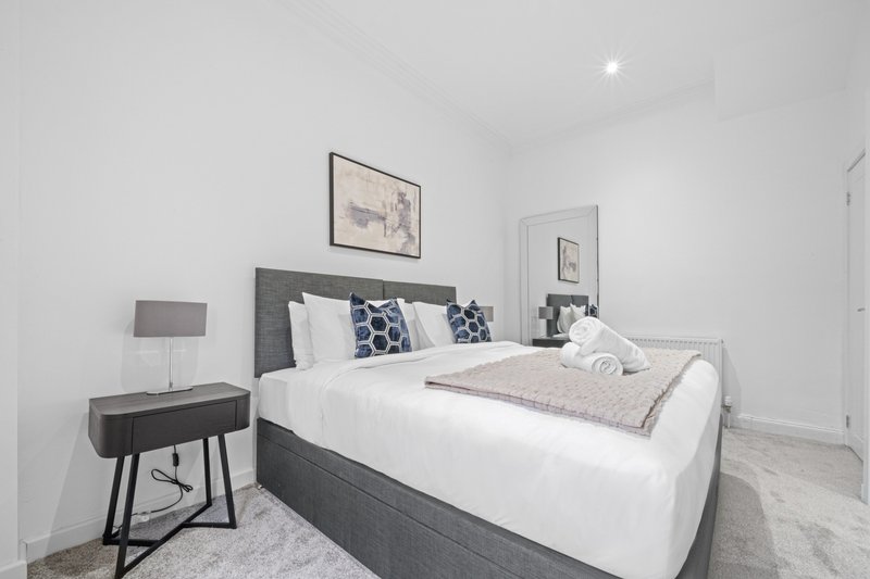 Modern bedroom with grey upholstered bed, white bedding, bedside table with lamp and framed wall art