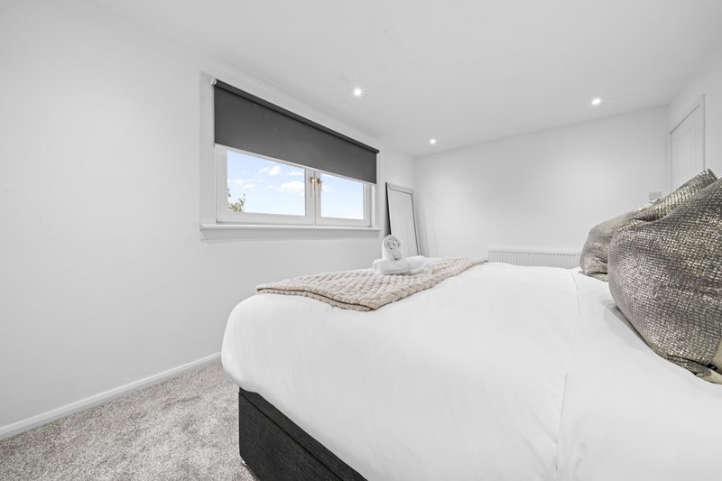 Modern bedroom with double bed, white bedding, grey throw blanket and window with dark blind