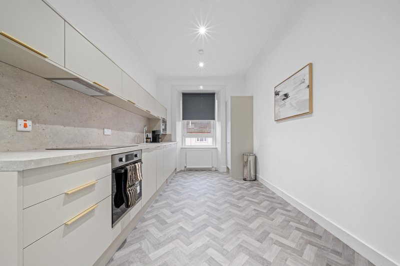 Modern galley kitchen with white cabinetry, herringbone floor, and appliances