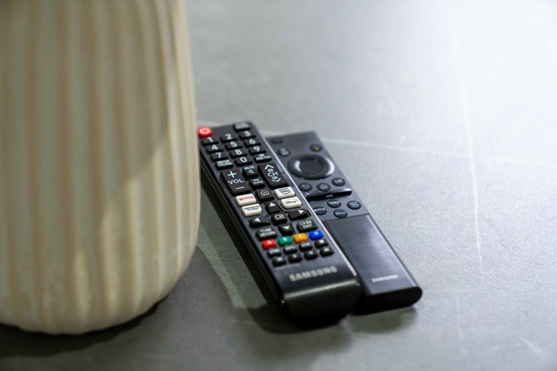 Two remote controls on a light surface next to a ribbed white lamp or vase
