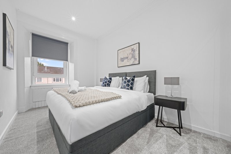 Modern bedroom with double bed, grey headboard, white bedding and side table