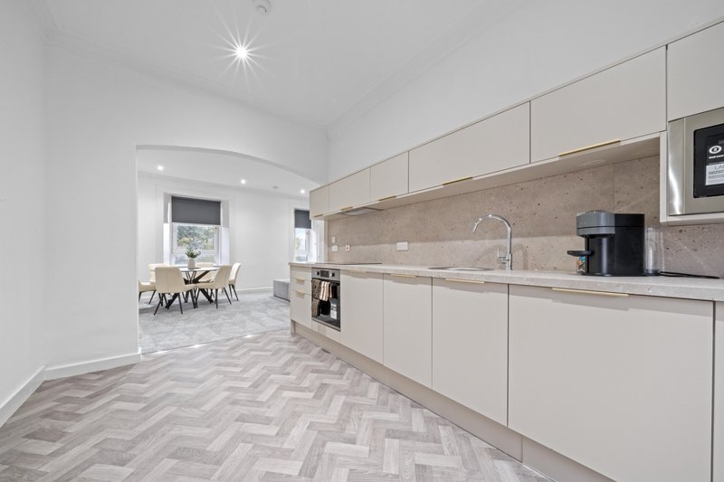 Modern kitchen with cream cabinets, stone backsplash, herringbone flooring and open-plan living area