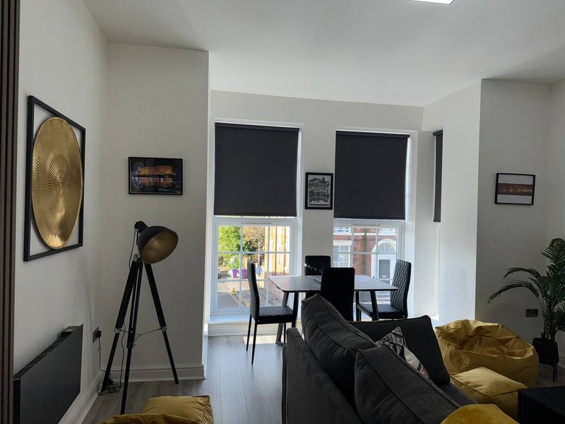 Modern living room with black sofa, yellow cushions, tripod lamp, and workspace area by windows